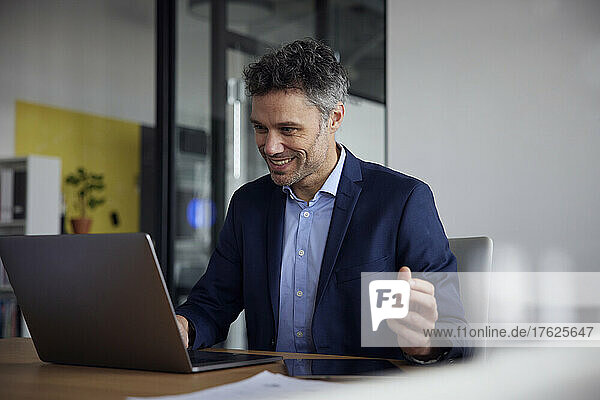 Happy businessman using laptop sitting at desk in office