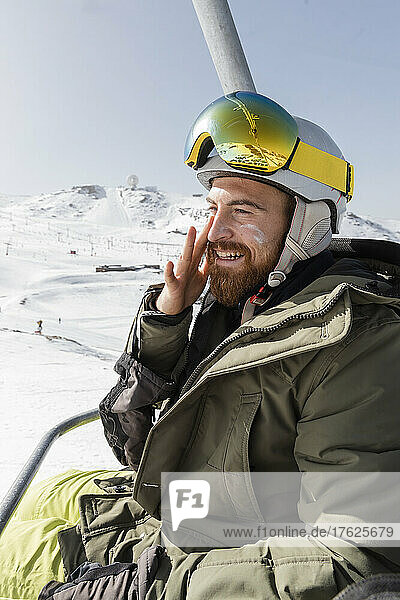 Lächelnder junger Mann  der am Skilift sitzend Sonnencreme aufträgt