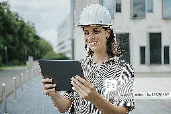 Lächelnder Architekt mit Schutzhelm nutzt Tablet-PC auf der Baustelle