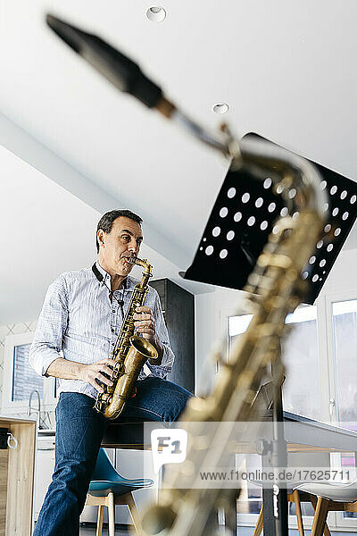 Musician playing saxophone sitting on table at home