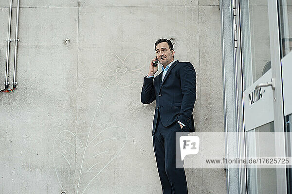 Businessman with hand in pocket talking on smart phone by wall in greenhouse