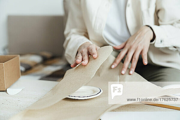 Craftswoman packing ceramic plate in wrapping paper for shipping