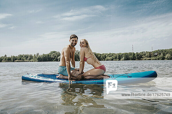 Happy couple sitting on paddleboard floating over lake