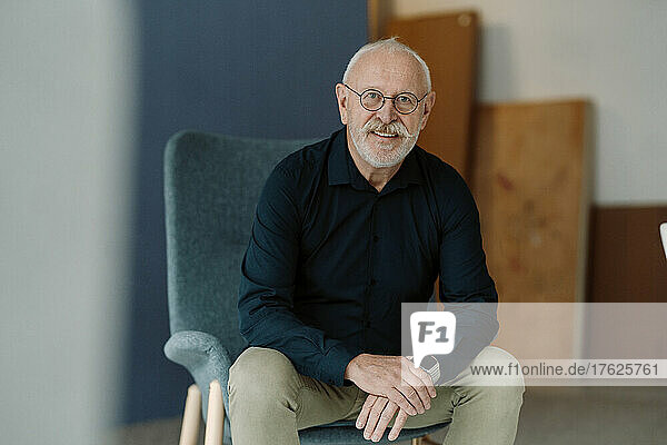 Smiling senior working man wearing eyeglasses sitting on chair in office