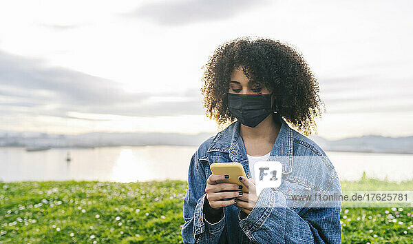 Woman with protective face mask using mobile phone in nature