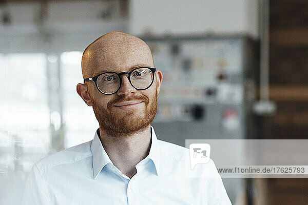 Smiling young bald working man wearing eyeglasses in office