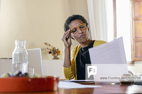Geschäftsfrau mit Brille prüft zu Hause Papierdokument