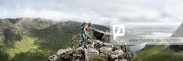 Woman wearing helmet climbing on top of rocky mountain