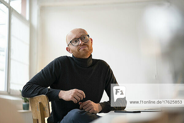 Thoughtful businessman wearing eyeglasses sitting in office