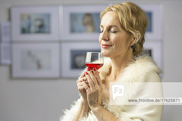 Smiling woman with wineglass standing at opening ceremony of exhibition