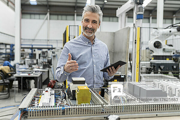 Smiling engineer holding tablet PC standing by machine in factory