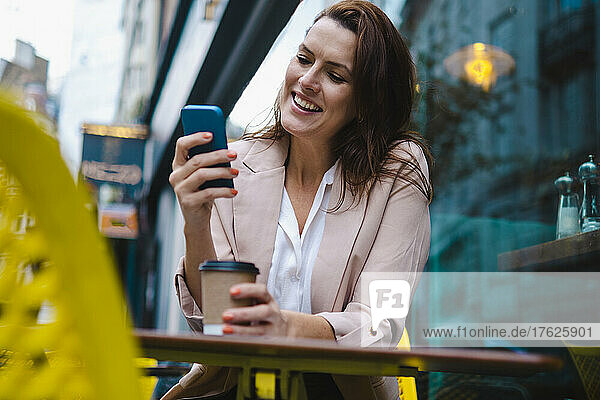 Happy woman using smart phone in sidewalk cafe
