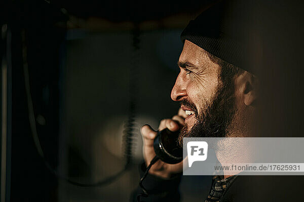 Happy man talking on telephone in control room of boat