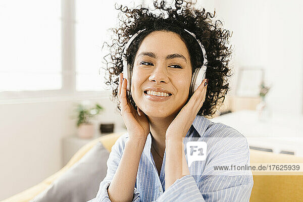 Glückliche Frau mit lockigem Haar  die zu Hause Musik über kabellose Kopfhörer hört