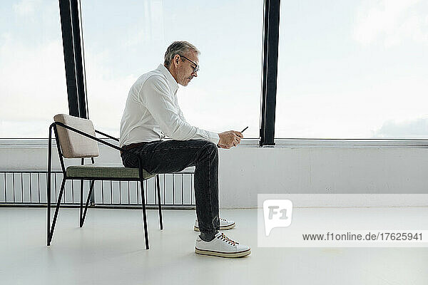 Businessman using smart phone sitting on chair at startup office
