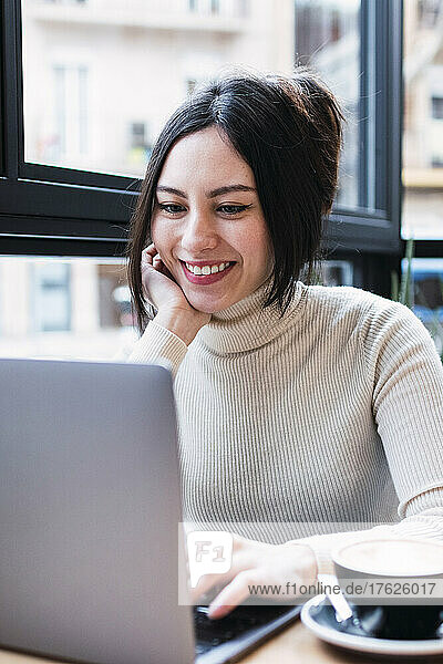 Smiling businesswoman using laptop sitting in cafe
