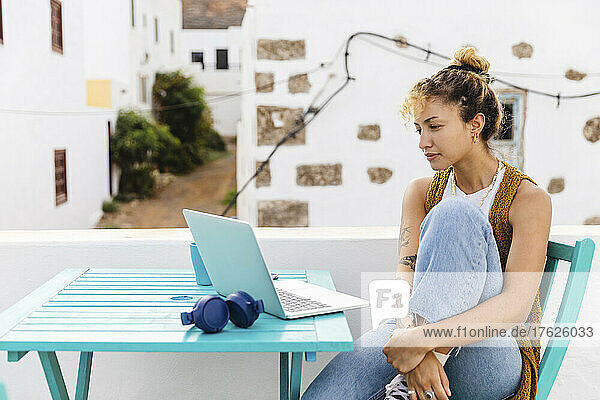 Young woman with laptop sitting at table on rooftop