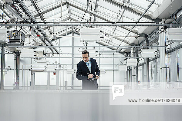 Businessman with tablet PC examining machinery in greenhouse