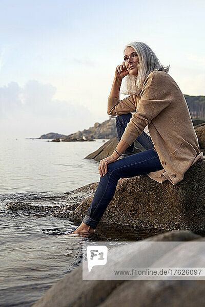 Gray haired woman sitting on rock at beach