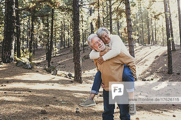 Lächelnder älterer Mann gibt Frau im Wald Huckepackfahrt