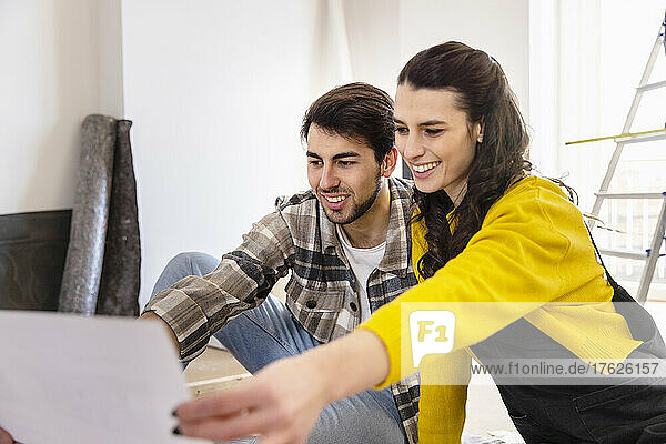 Lächelnde Frau diskutiert mit ihrem Freund im Wohnzimmer über Grundrisse