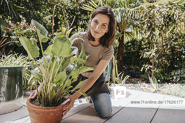 Smiling gardener holding potted plant in garden