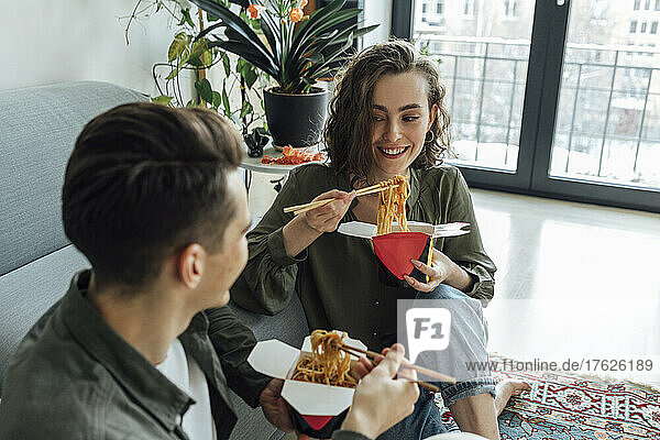 Happy woman and man with take out food talking in living room at home