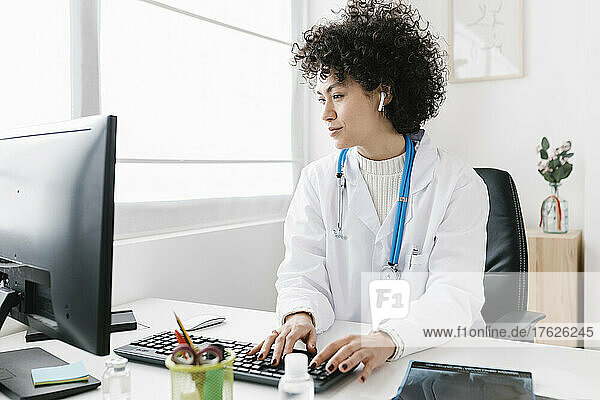Doctor wearing in-ear headphones using desktop PC at medical clinic