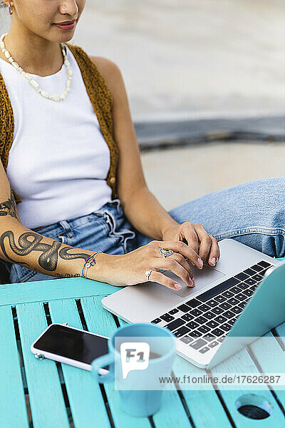 Young woman with tattoo typing on laptop sitting at table