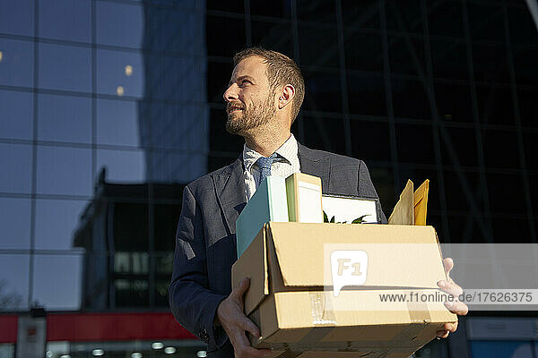 Businessman carrying box full of belongings for office on sunny day