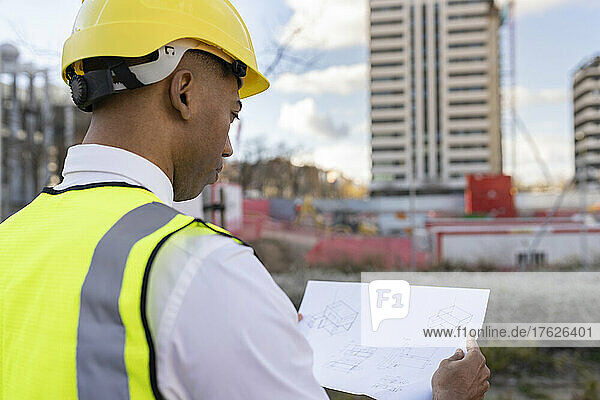 Architect wearing hardhat reading blueprint at construction site
