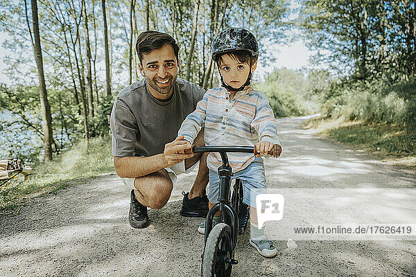 Smiling father and son with cycle on road