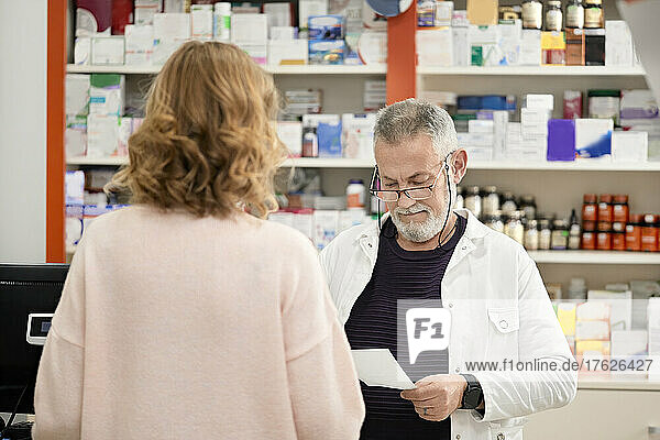Pharmacist reading prescription standing with customer at checkout counter in pharmacy store