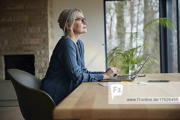 Blonde Frau mit Brille sitzt mit Laptop am Tisch