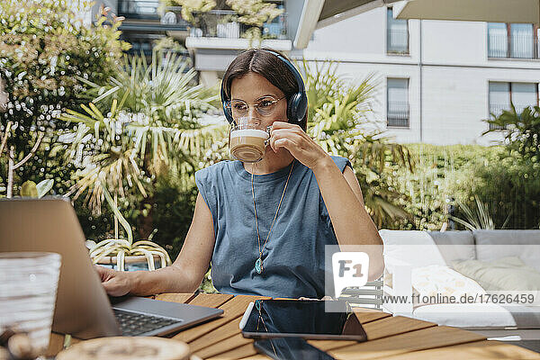 Geschäftsfrau trinkt Kaffee und arbeitet im Garten am Laptop