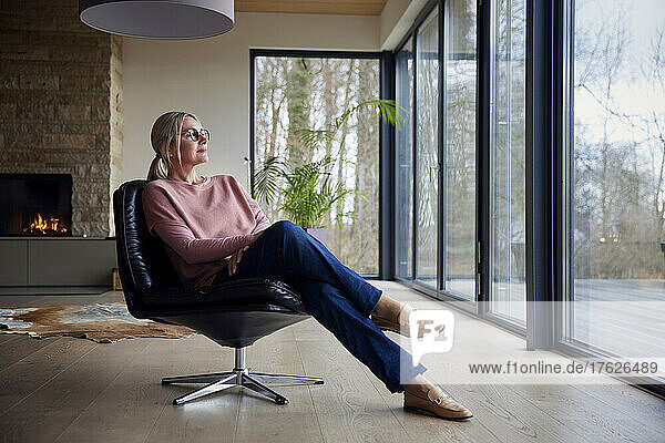 Woman looking through glass window sitting on chair in living room