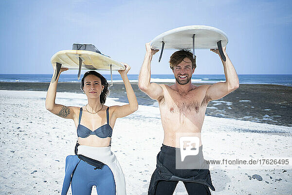 Happy couple carrying surfboard at beach on sunny day
