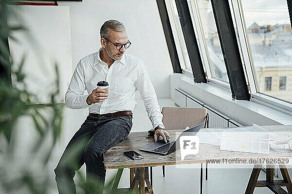 Businessman using laptop sitting on desk in office