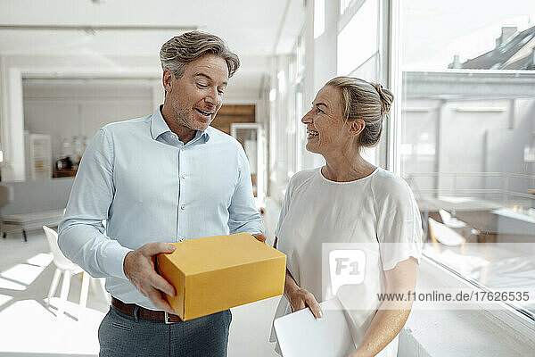 Businessman holding box discussing with happy businesswoman in office