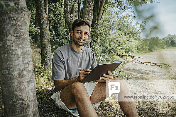 Smiling man with tablet computer sitting in nature