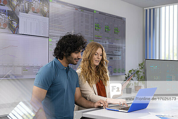 Geschäftsfrau benutzt Laptop und diskutiert mit Techniker am Schreibtisch im Kontrollraum