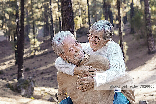 Happy senior man giving piggyback ride to woman in forest