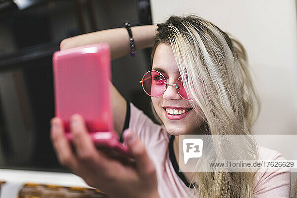 Happy blond teenager with hand in hair looking at mirror