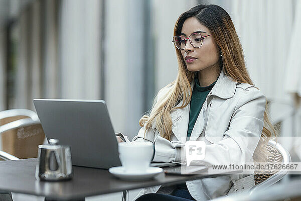 Freelancer working on laptop sitting at sidewalk cafe