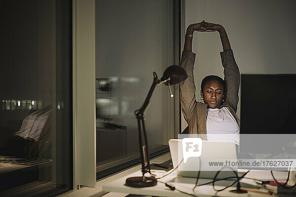 Müde Geschäftsfrau  die ihre Hände bei der nächtlichen Arbeit im Büro ausstreckt