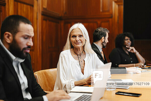 Portrait of smiling businesswoman sitting by businessman using laptop at conference table in board room
