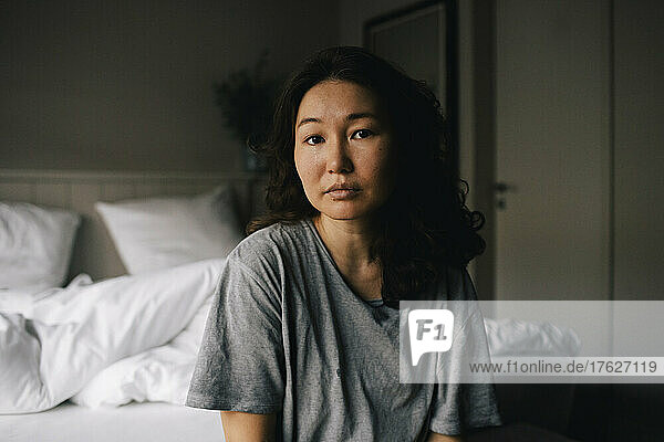 Porträt einer traurigen  psychisch kranken Frau  die zu Hause im Schlafzimmer sitzt