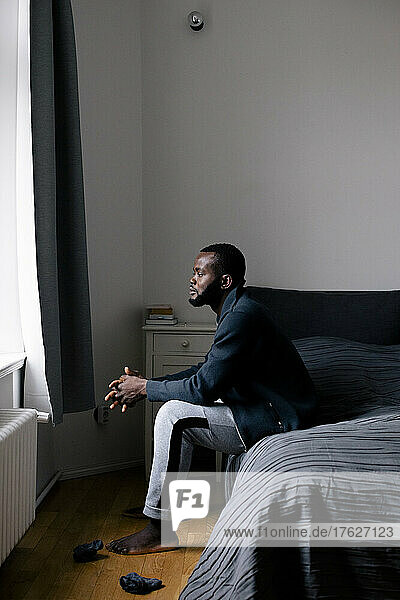 Volle Länge Seitenansicht von nachdenklichen Mann sitzt auf dem Bett zu Hause