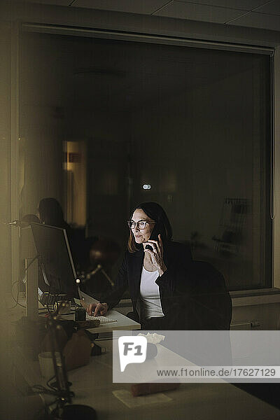 Reife Geschäftsfrau  die mit ihrem Smartphone telefoniert  während sie noch spät im Büro arbeitet