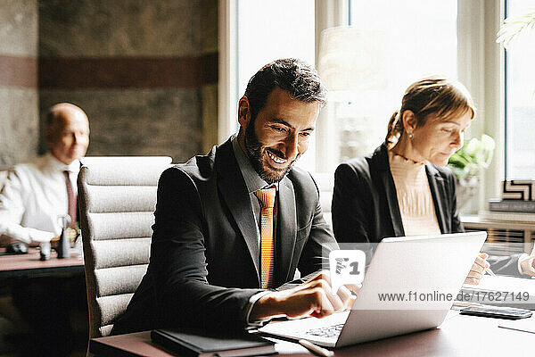 Lächelnder Geschäftsmann  der einen Laptop benutzt und mit einer Geschäftsfrau am Schreibtisch in einer Anwaltskanzlei arbeitet